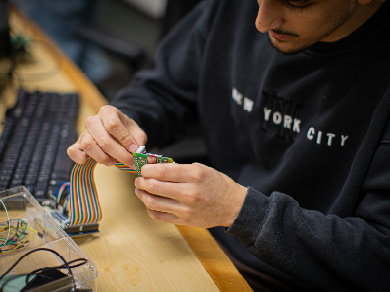 Malik sitting at a desk holding parts for the Raspberry Pi cluster.