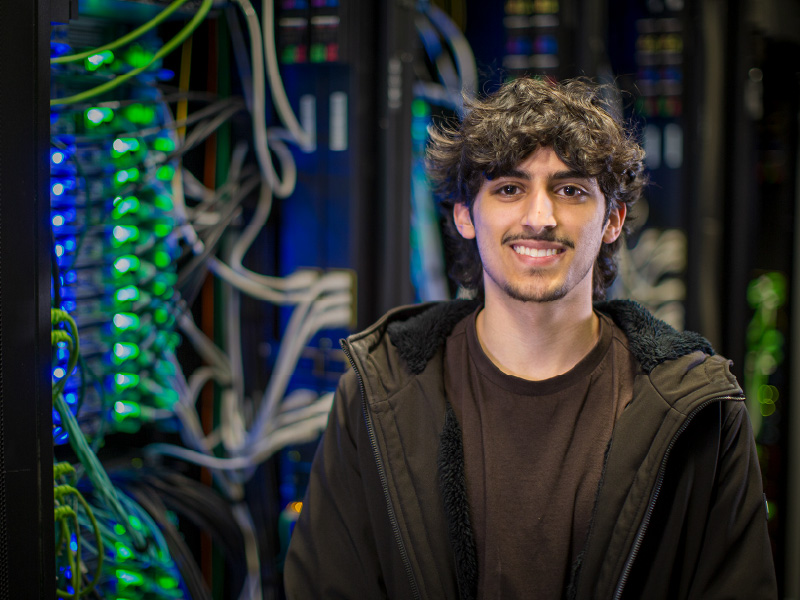 Malik standing in front of blue and green lights and white wires. 