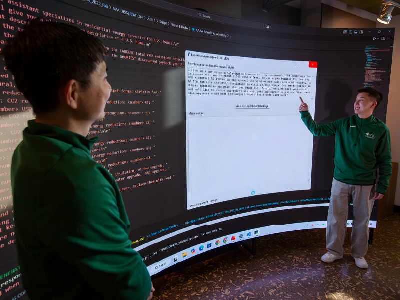 Dong Zhao and Lei Shu standing in front of a large screen displaying code.