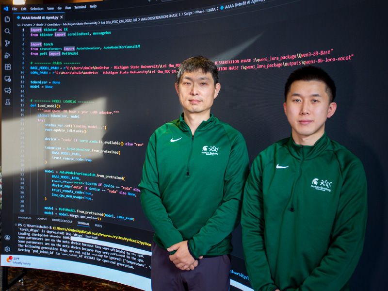 Dong Zhao and Lei Shu standing in front of a large screen displaying code
