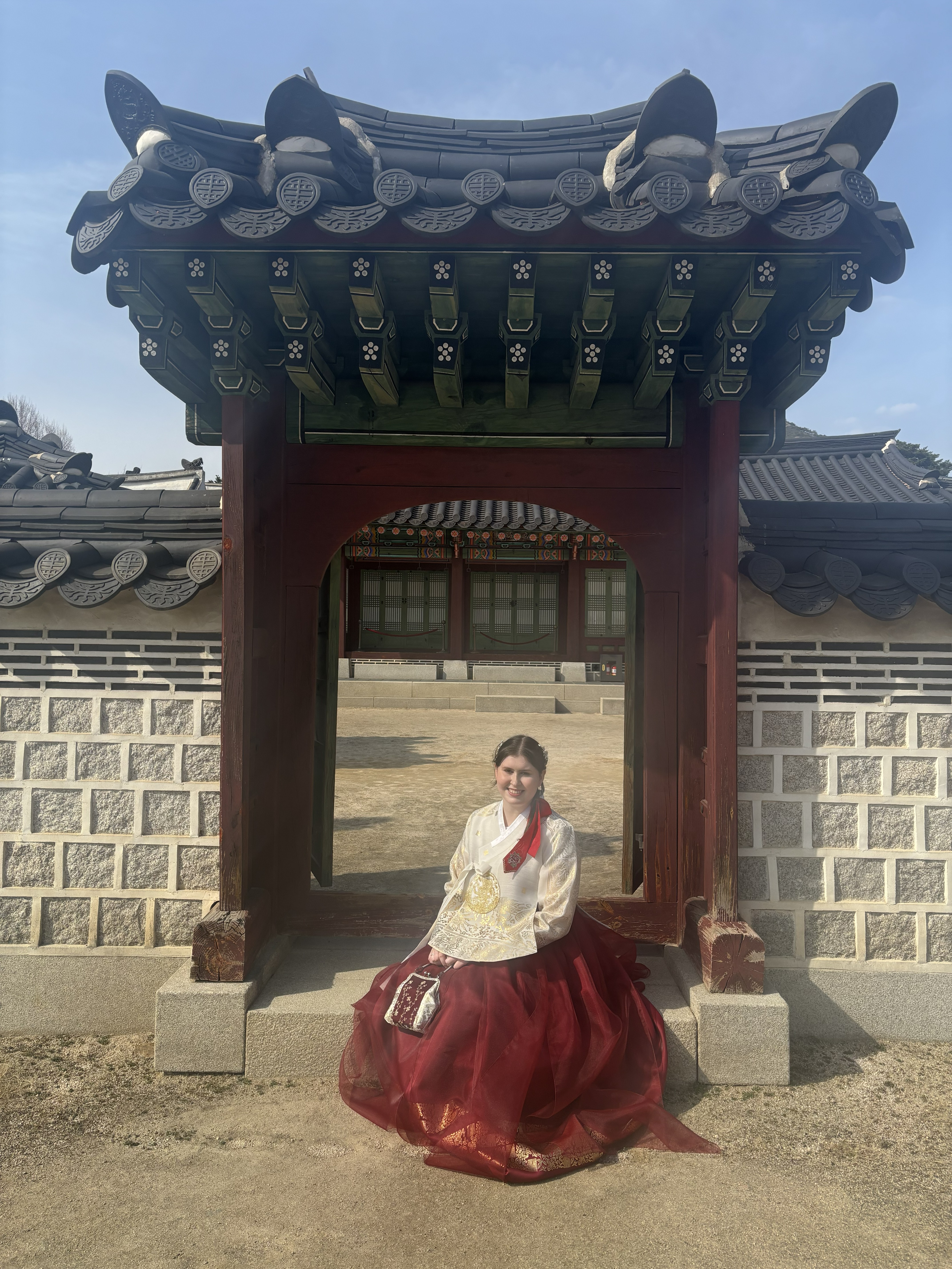 Catelyn Arnold wears a traditional Korean hanbok while seated beneath a palace gate in South Korea.