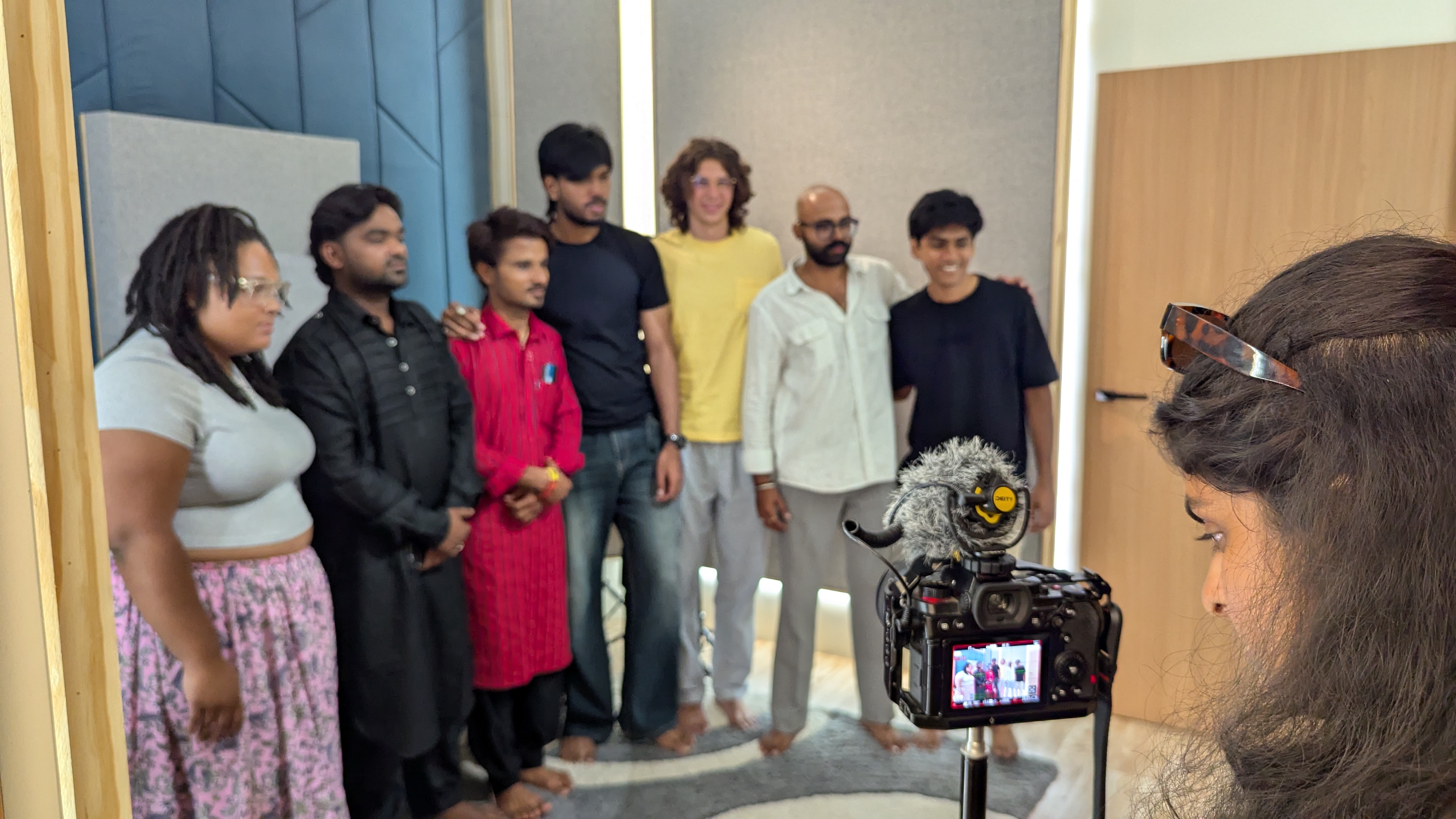 A group of students and local participants stand together for a photo while a person films them with a camera.