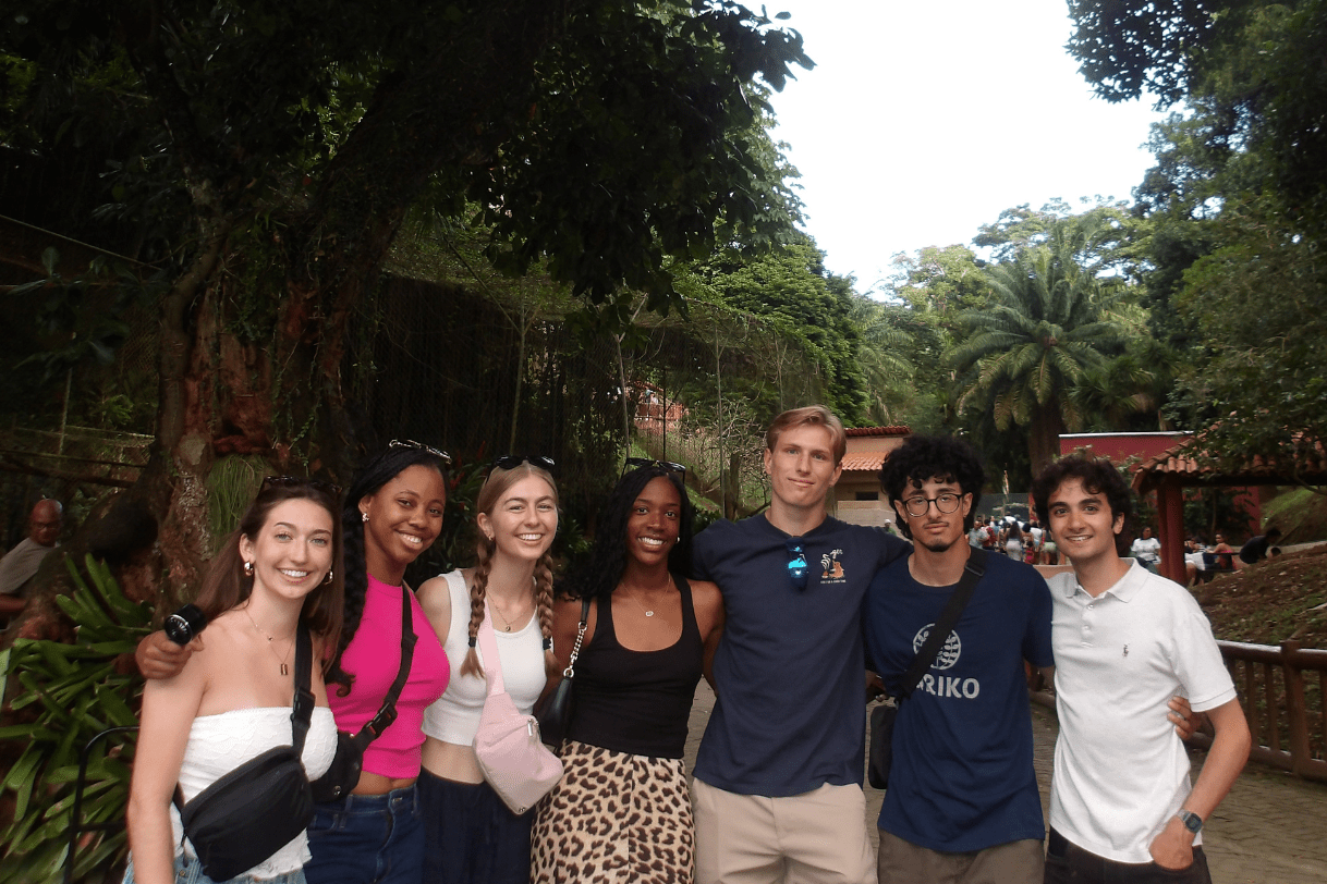 A group of seven university students posing together outside in Brazil in front of lush greenery.