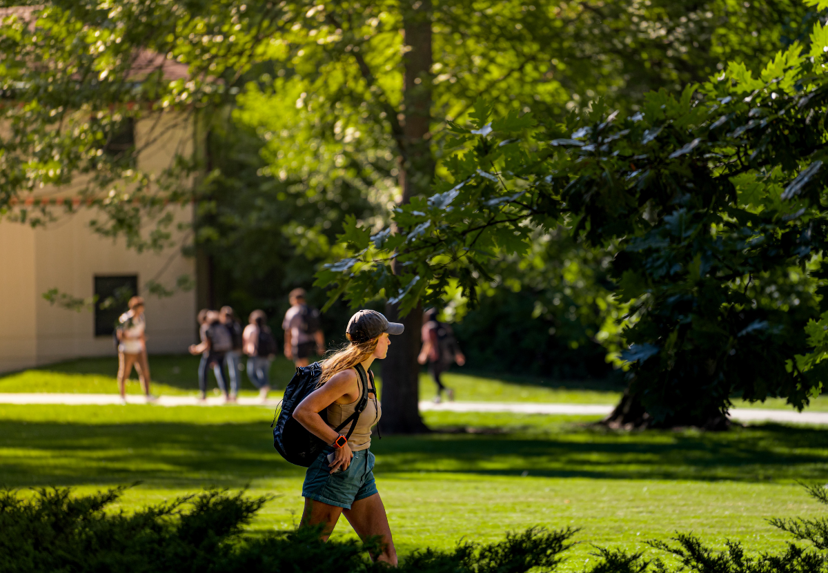 A student wearing a baseball cap and backpack walking around MSU campus.