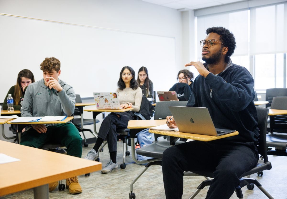 James Madison College student participating in a classroom discussion while classmates work on laptops during a university lecture.