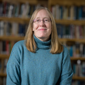 JMC Prof. Susan Stein-Roggenbuck photographed in the JMC Library wearing a blue sweater and glasses.