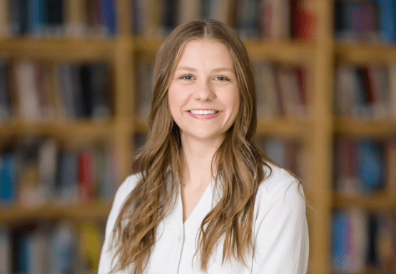 This photo shows Madeline Chryczyk posing in front of a background of blurred bookshelves in the JMC Library.