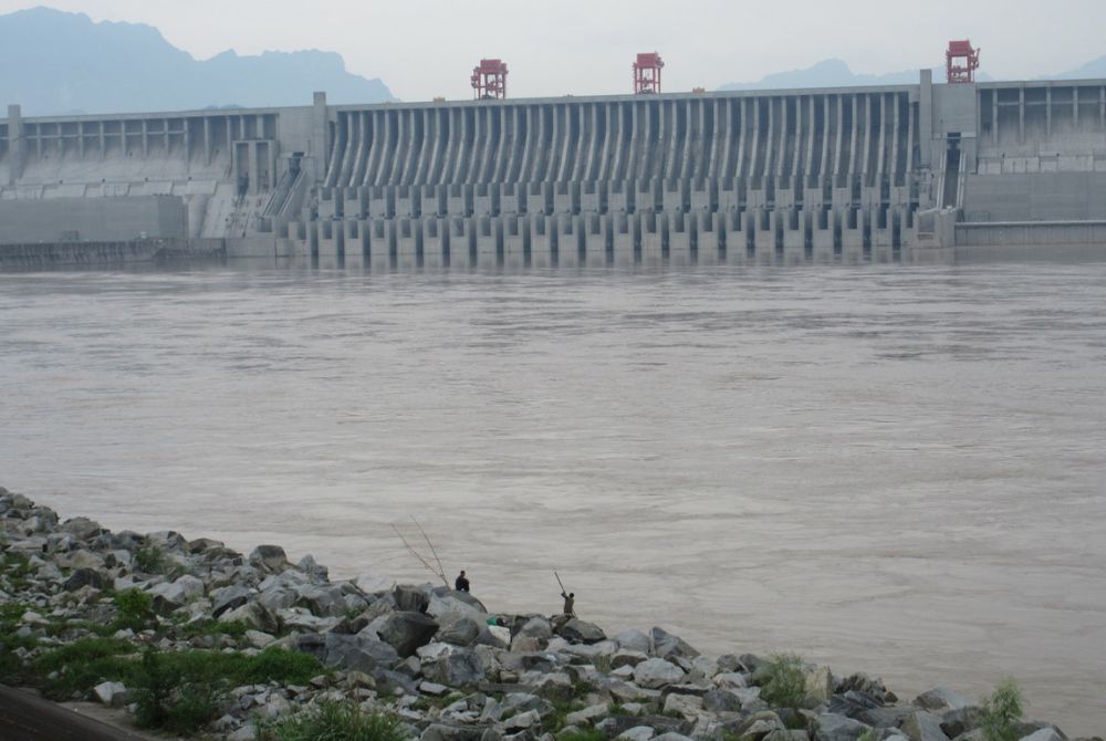 Large hydropower dam with two fisherman in the bottom section of the photo.