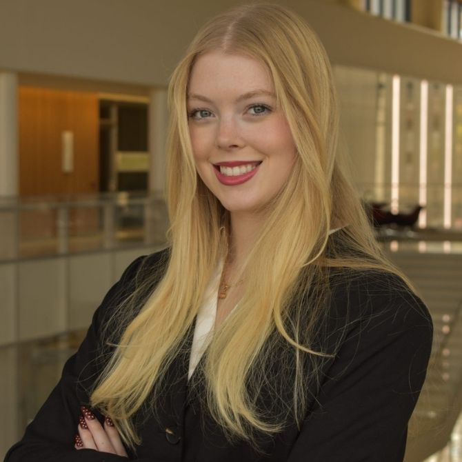 Professional portrait of a JMC student, smiling at the camera with arms crossed. Student is wearing a black blazer.
