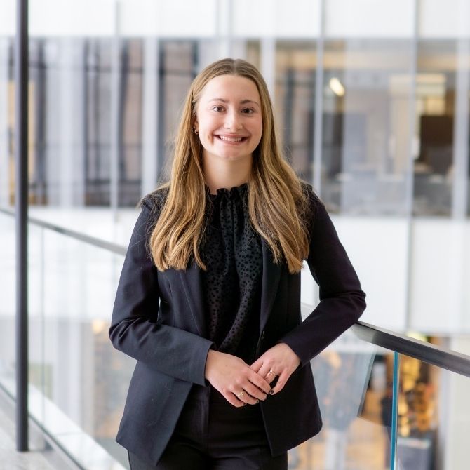 JMC student wearing a black blazer and black shirt. Walls of glass windows are visible behind the student.