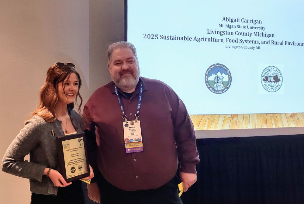 Abigail Carrigan presented with the American Planning Association award on April 27, 2026. She is holding a plaque, standing with the Chair of the American Planning Association - Small Town & Rural Planning Division. 