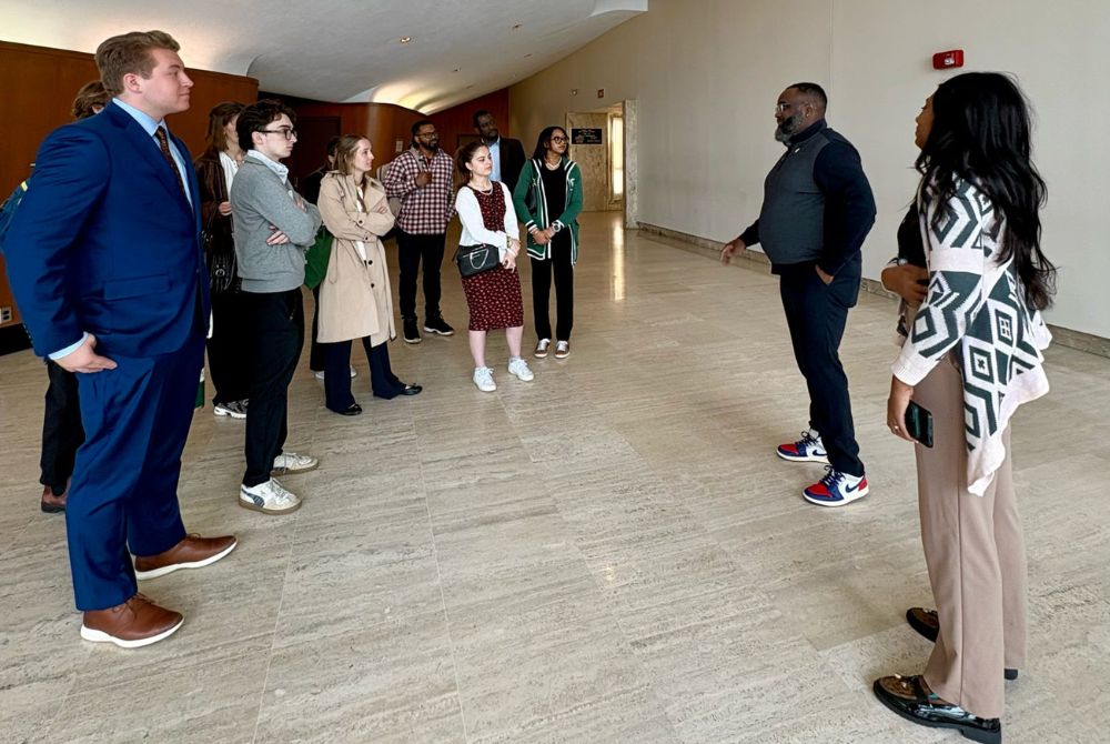 JMC students listen as two professionals address them in the curved lobby of a Detroit building during a career site visit.