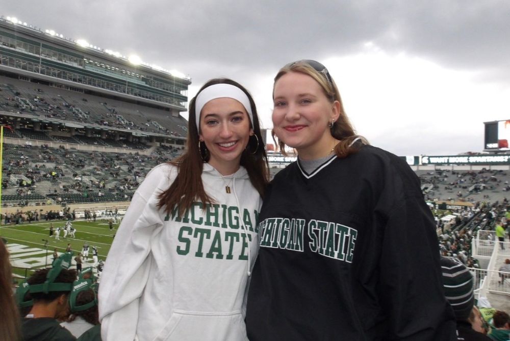 Finni Padgitt photographed at an MSU Football game with her sibling. They are both wearing Michigan State sweatshirts.