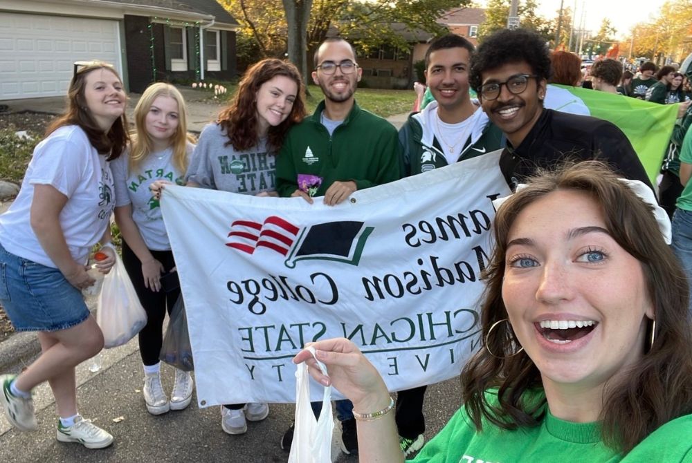 Finni Padgitt taking a selfie with a group of six other JMC students. They are holding a banner that reads James Madison College Student Senate.