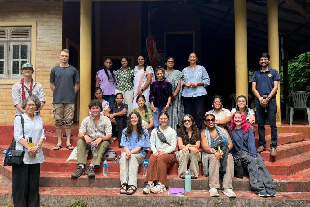 A group of students, faculty, and community members pose together on the steps of a building during a study visit.