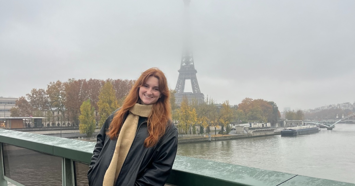 Photo of Isabelle Radakovich, standing at a distance in front of the Eiffel Tower.