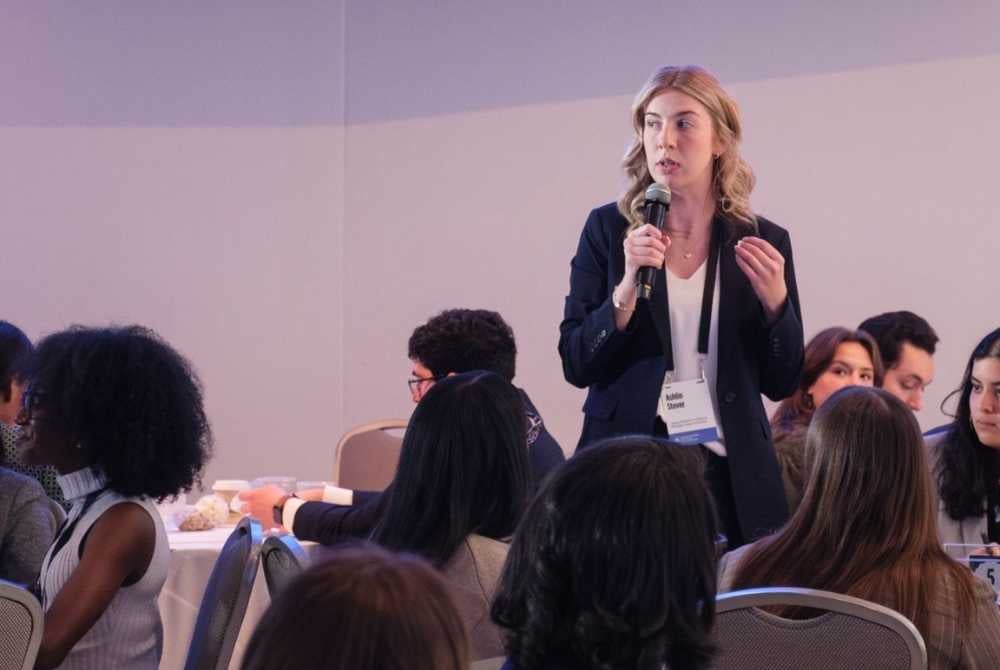 JMC student speaking at the Obama Foundation Fall Summit. She is in a conference room, wearing a black blazer and holding a microphone.