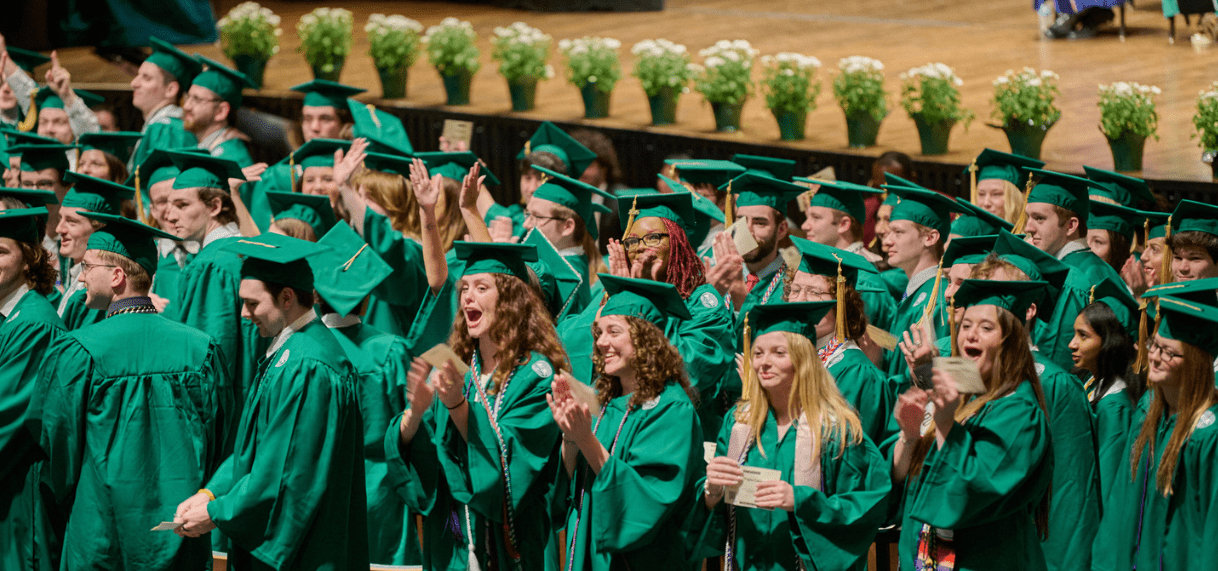 A group of JMC students wearing green caps and gowns during the college's annual commencement ceremony in the Wharton Center.