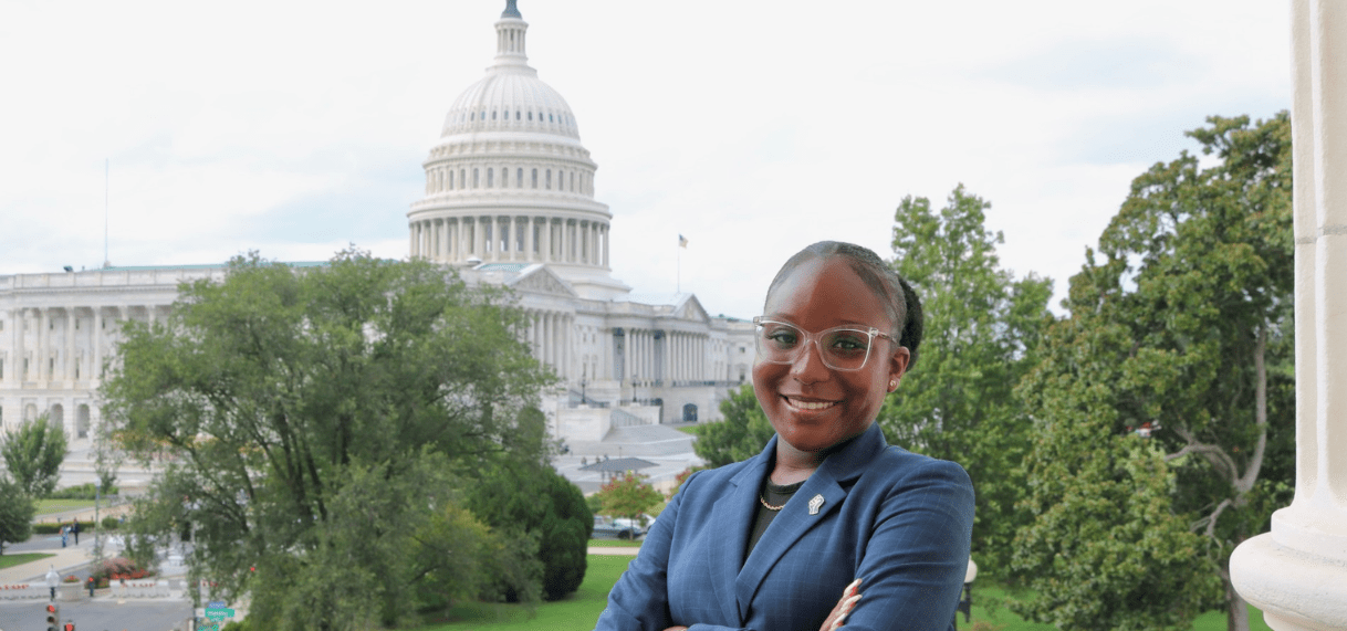 A JMC student is standing in front of the United States Capitol building during her internship, as part of JMC's field experience requirement. She is wearing a blue blazer and posing with her arms crossed.