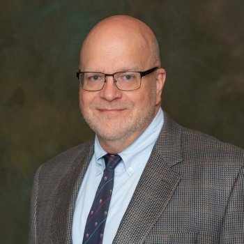 Headshot of John Jackson wearing glasses and a plaid blazer. 