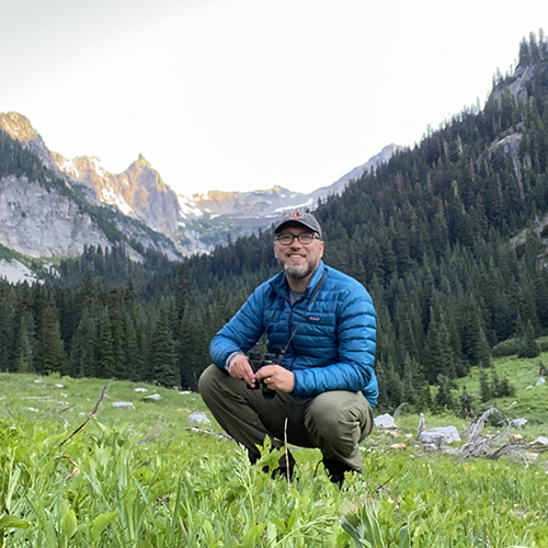 man standing in green grass with mountain landscape behind