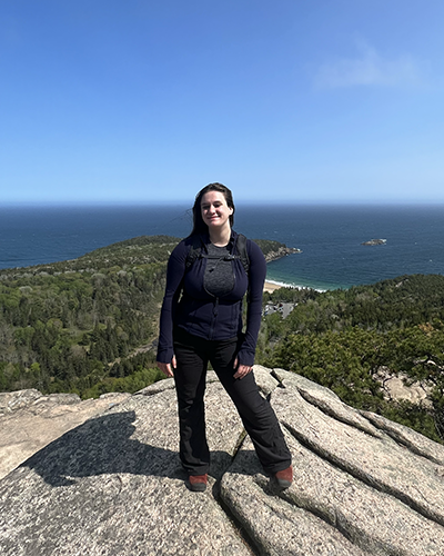 Claire Smith standing on top of rocky mountain overlooking water