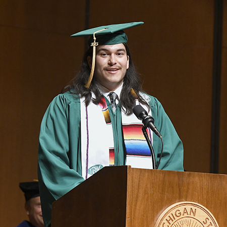 Ian Earle dressed in cap and gown at podium