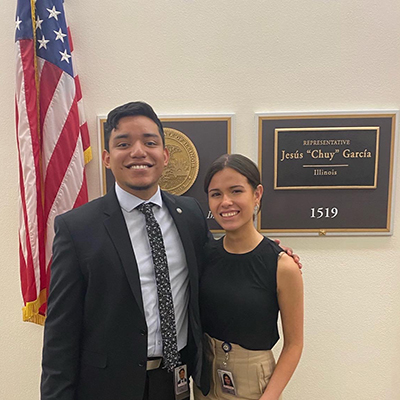 two people standing beside one another with an American flag in the background and a sign for a U.S. Representative's office