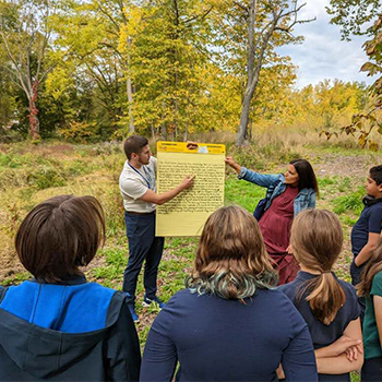 students standing outside looking at a teacher holding a large pad with writing