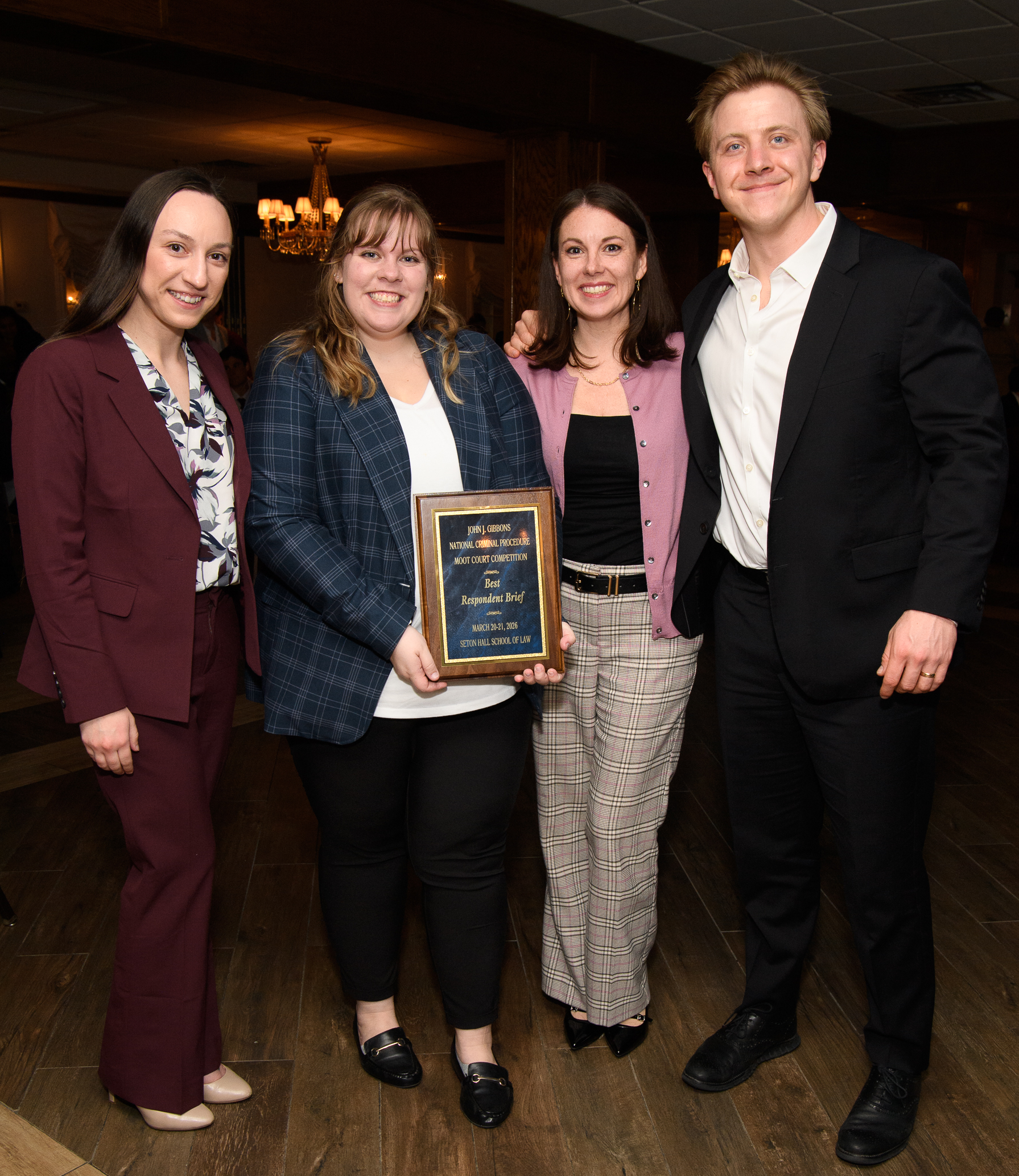 Four law students pose at an indoor awards event, smiling as one holds a plaque for “Best Respondent Brief” from the John J. Gibbons National Criminal Procedure Moot Court Competition at Seton Hall School of Law.