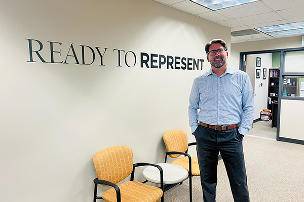 Bradley Hall, Interim Director of MSU Law’s new Public Defender Clinic standing in front of a wall with a graphic of 'Ready to Represent' on it.