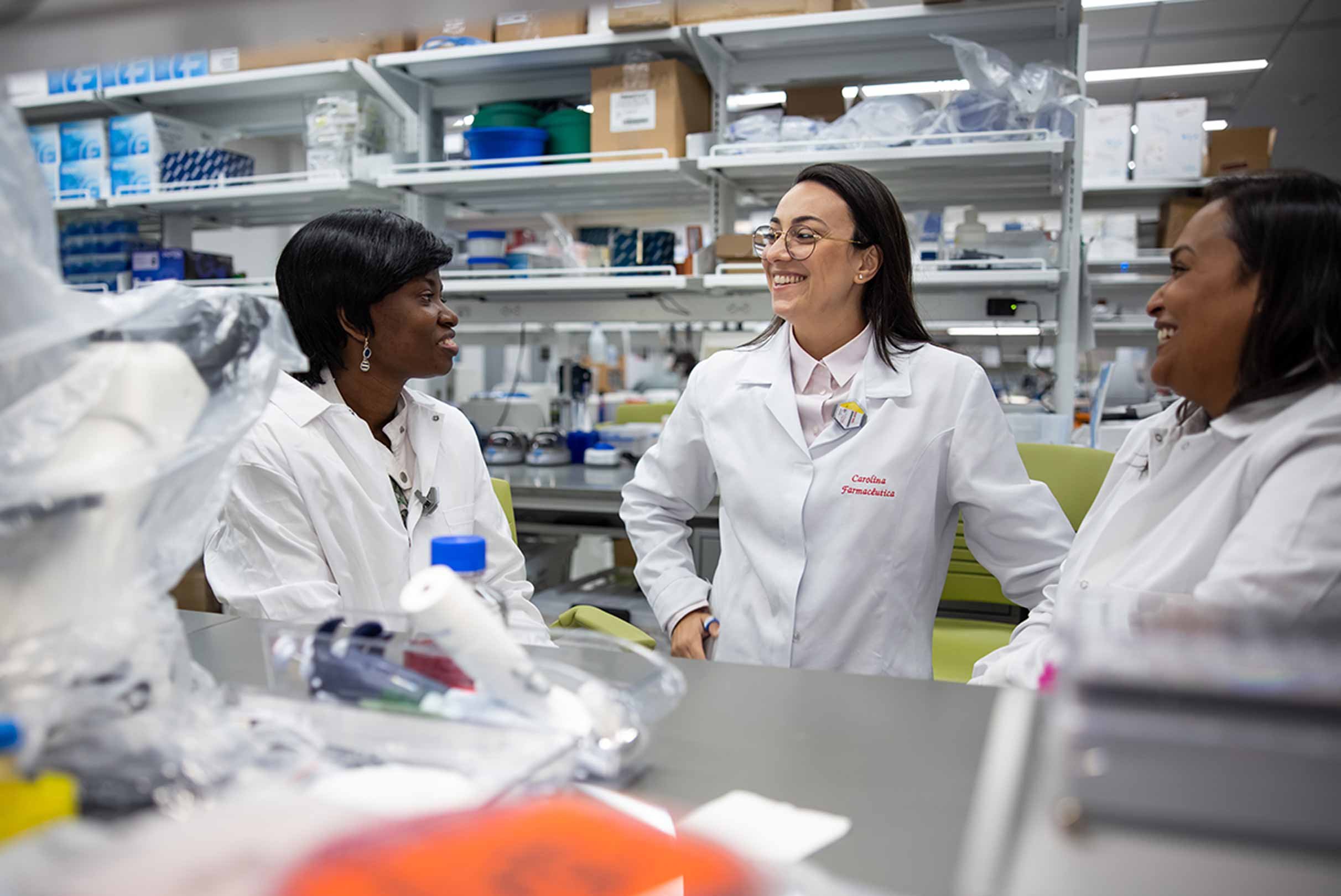 Three individuals in lab coats sharing a conversation and a laugh in a well-equipped laboratory setting.