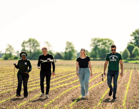 Michigan State University students and researchers conducting sustainable agriculture research in a crop field using drone technology and soil analysis tools.