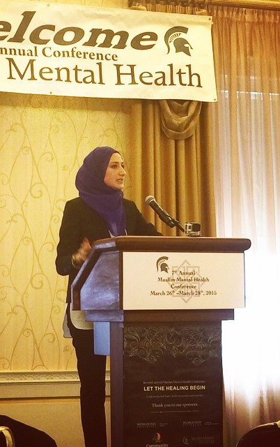 A woman stands behind a podium to speak at the 7th Annual Muslim Mental Health Conference.
