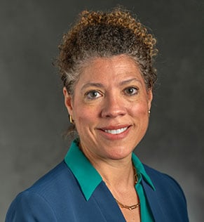 Headshot of Amy Hertel, smiling, wearing a green blouse and a navy suit jacket. 