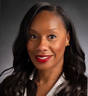 Ashley Green, smiling, wearing a black suit with a pinstriped blouse.