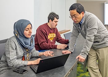 two people on laptops sitting while third person stands in front of them to answer questions