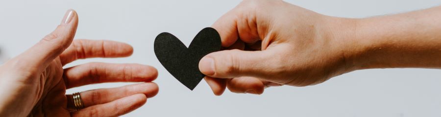 One hand holds a black heart out to another hand