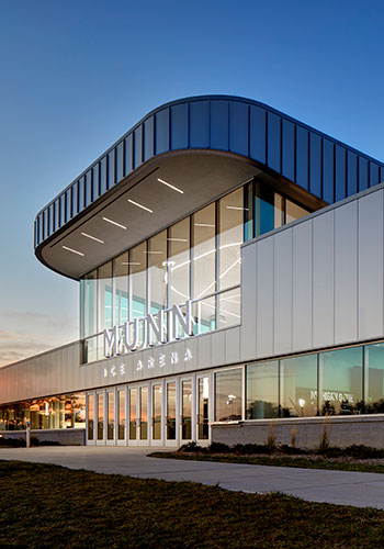 the new south entrance of Munn Ice Arena, featuring the glass and metal facade, lit from within, at dusk