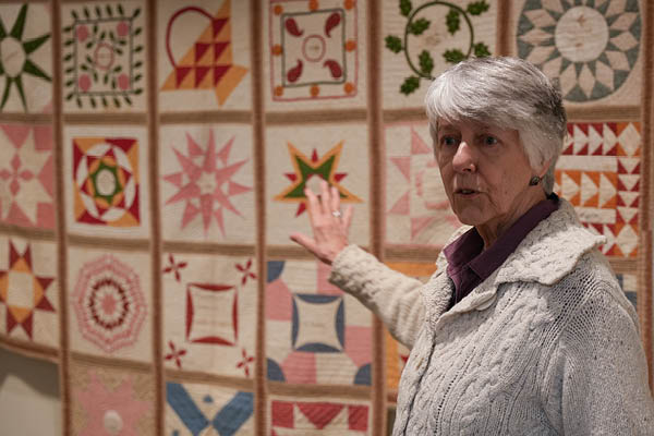 MSU alumna Christine Force gestures toward a colorful quilt display while speaking during an exhibition at the Maine Historical Society.