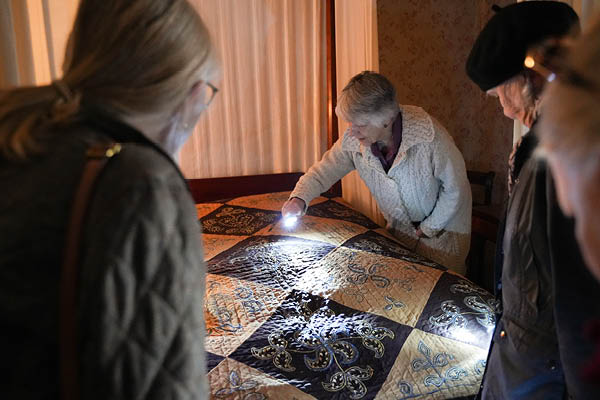 MSU alumna Christine Force holds up a flashlight to inspect the detail close up on the Delphos Turner quilt while it lies on a bed as part of an exhibition at the Maine Historical Society.
