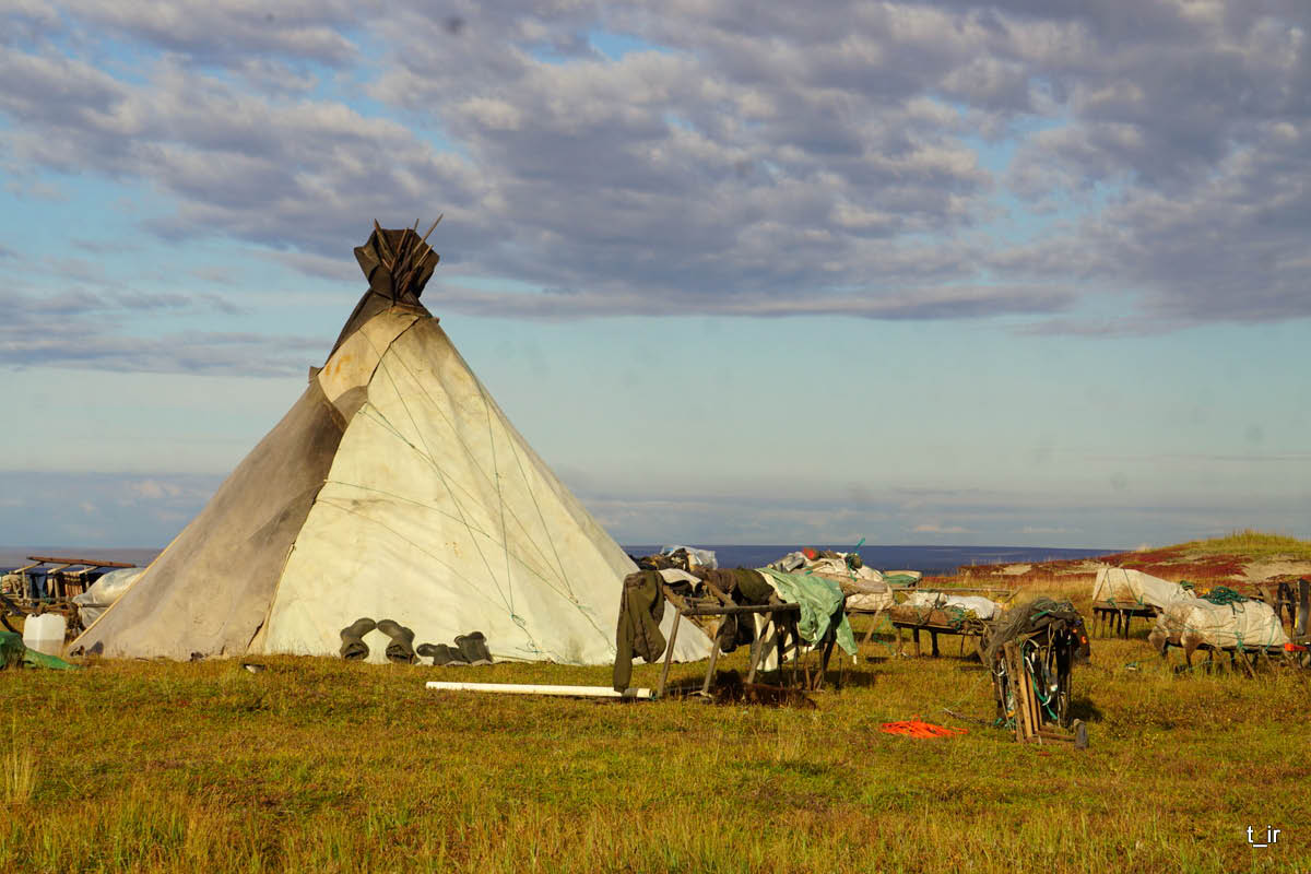 A Native American teepee and items on a grassy plain under a cloudy sky.