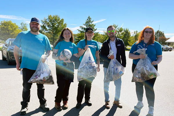 Five employees from Sea Life Michigan Aquarium stand together each holding bags of trash collected during a volunteer watershed cleanup.