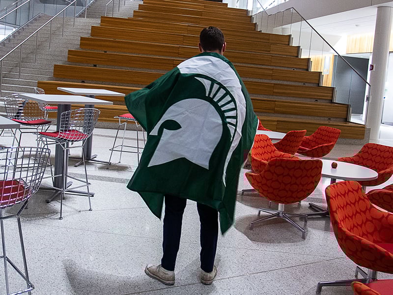 Student facing away from camera with Spartan flag draped around back