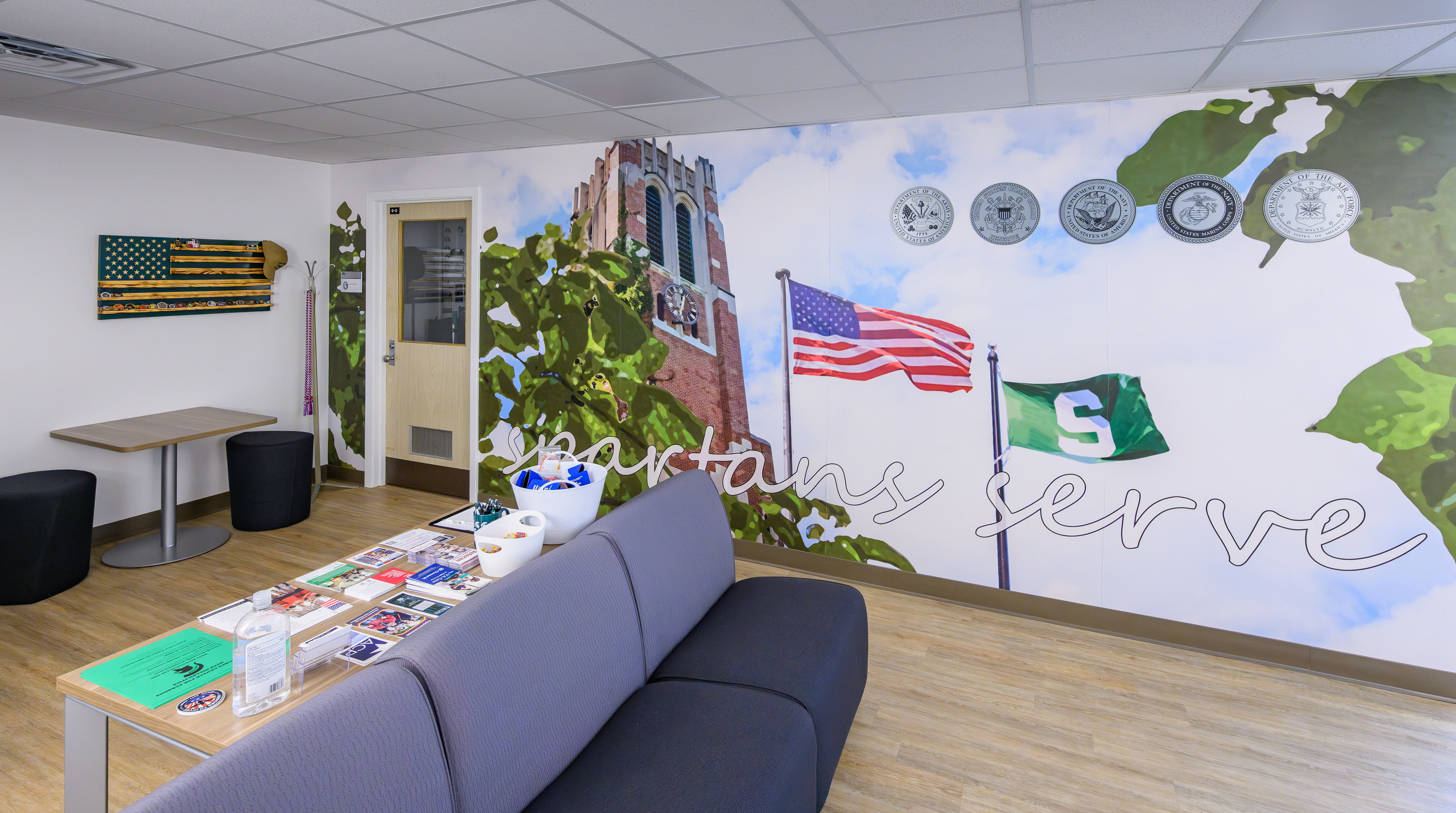 A welcoming lounge inside the Center for Veterans and Military-Affiliated Students, featuring a mural with U.S. and MSU flags, military branch emblems, and the words, Spartans Serve.