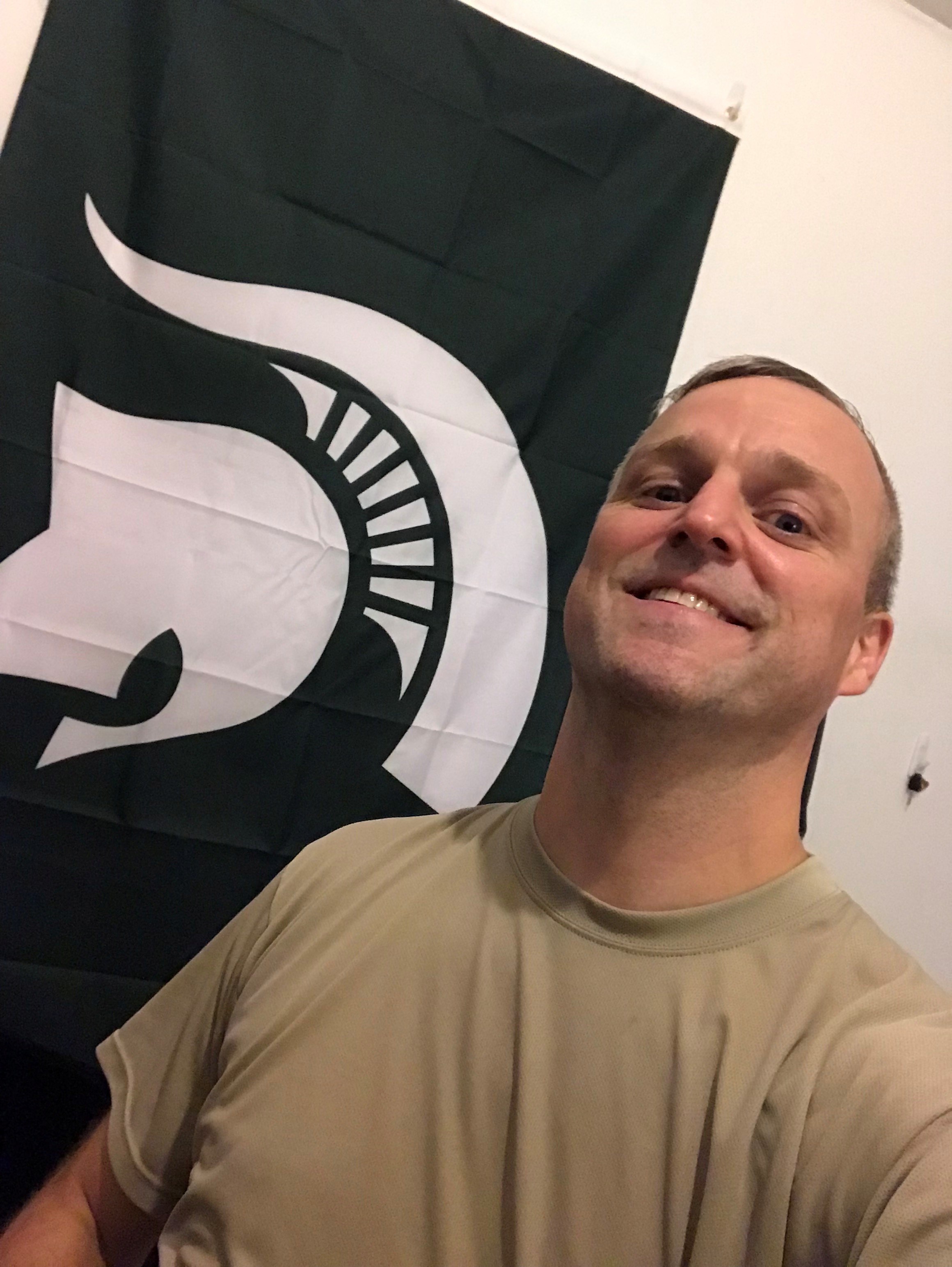 Joe Funston III, '03, poses with the Spartan flag while on assignment in Qatar.
