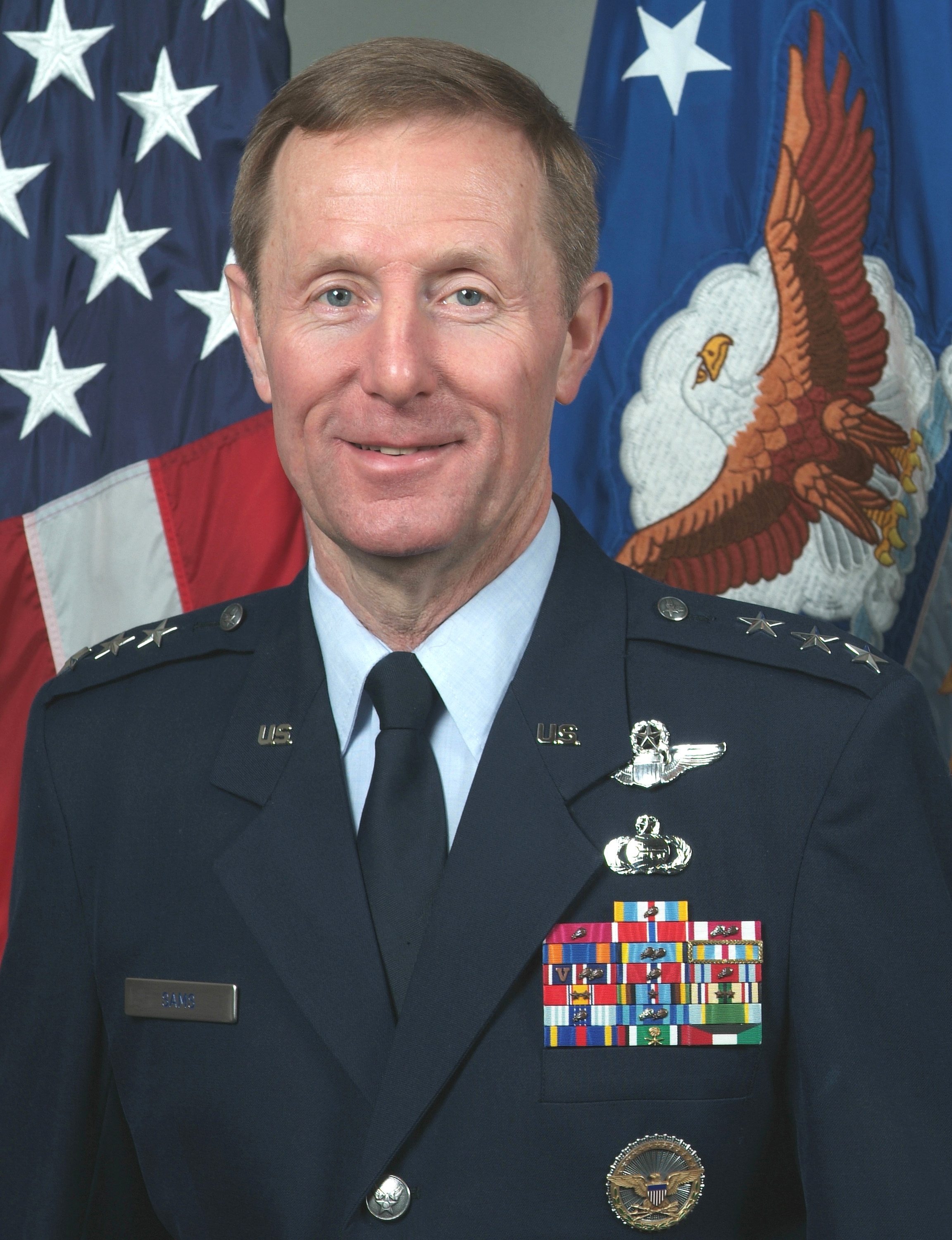 Official portrait of Lieutenant General Ronald F. Sams in uniform, standing before American and Air Force flags.