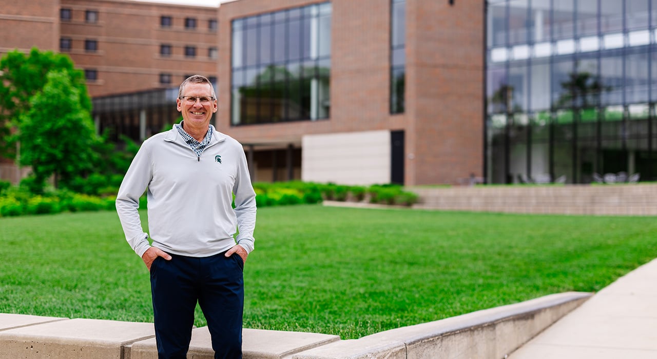 Penegor wearing a Michigan State University pullover standing outside a modern campus building with green lawn.