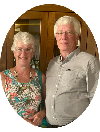 A head-and-shoulders portrait of Sandy Cottingham and her husband Steve Cline. Sandy is wearing a flowered dress, Steve is wearing a light-colored button-up shirt. 
