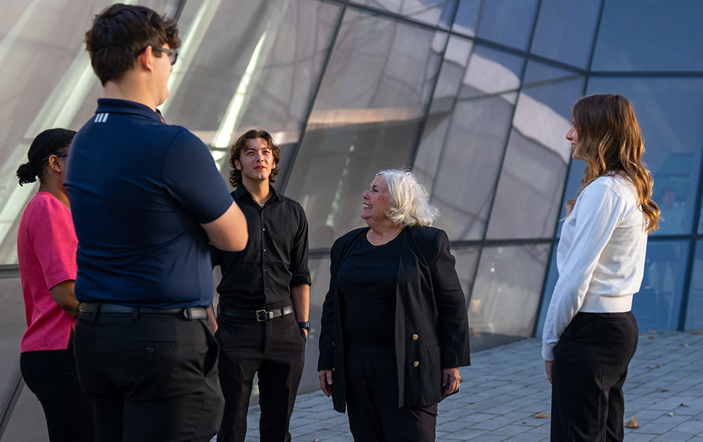Lou Ann Tompkins stands outdoors in a semi-circle of MSU students